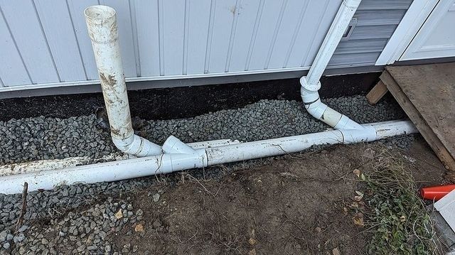 Vita markrör och stuprör längs husgrund med grus och bar mark