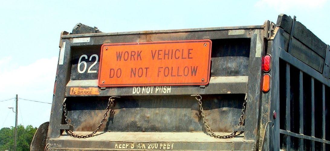 Bakdelen på en tipptruck för byggarbetsplatser med en orange varningsskylt 'WORK VEHICLE DO NOT FOLLOW'.