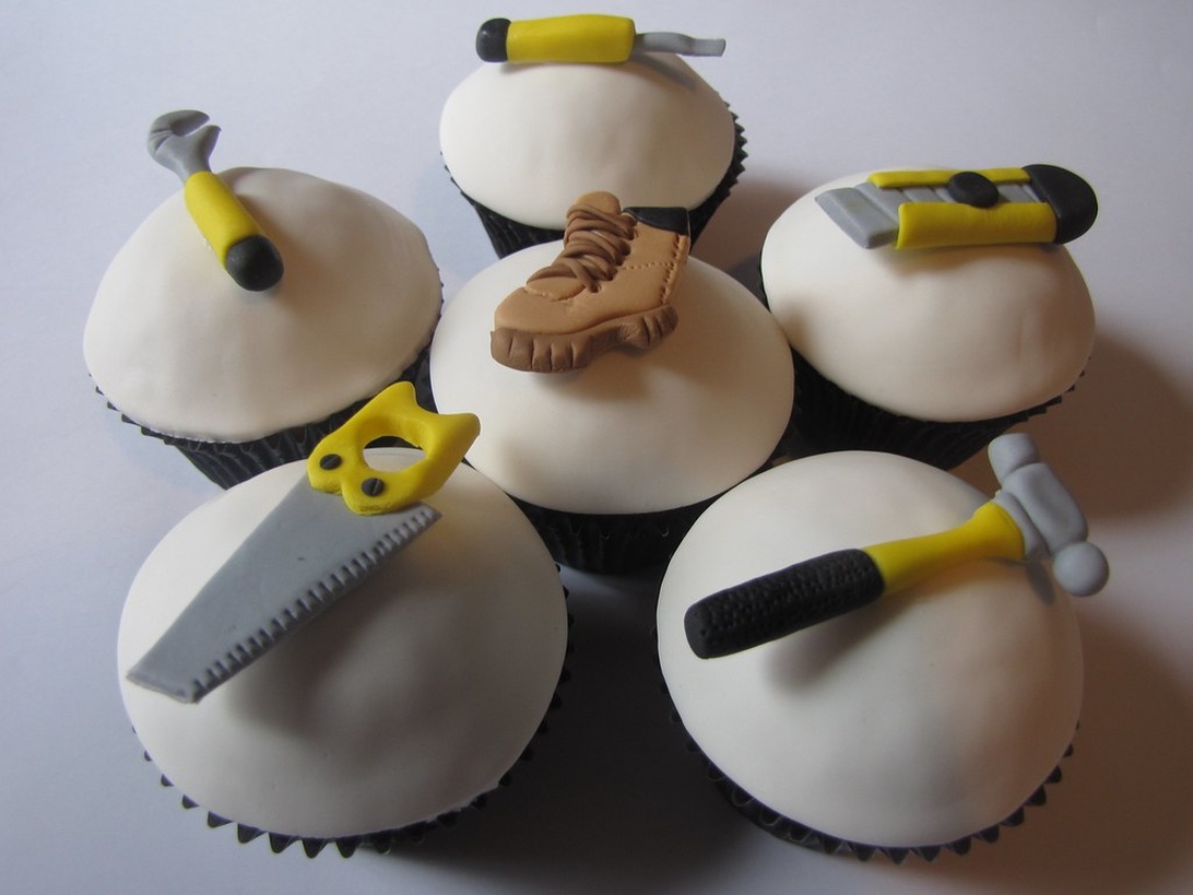 Sex cupcakes med vit glasyr och sockerdekorationer formade som olika verktyg.
